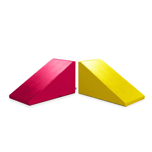 Two colorful Mega Wedge Play Triangles by Foamnasium are shown against a white background, one in bright red and the other in vibrant yellow. These durable foam playsets are typically used for physical therapy, gymnastics training, or children's play areas to help with exercises and movement activities.