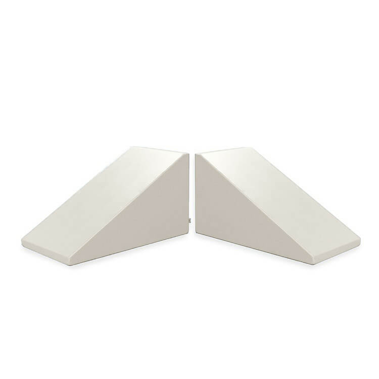 Two Mega Wedge Play Triangles by Foamnasium, GREENGUARD GOLD Certified, are arranged with their angled sides facing each other, creating a symmetrical appearance. These white triangular foam wedges are likely used for support or positioning. The background is plain white.