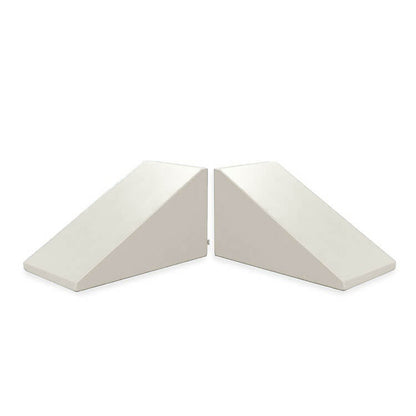 Two Mega Wedge Play Triangles by Foamnasium, GREENGUARD GOLD Certified, are arranged with their angled sides facing each other, creating a symmetrical appearance. These white triangular foam wedges are likely used for support or positioning. The background is plain white.