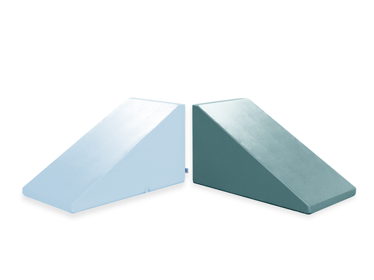 Two Foamnasium Mega Wedge Play Triangles are shown side by side against a white background. The one on the left is pale blue, while the one on the right is dark green. Both have a sloped design that tapers to a point, likely for support or elevation purposes. These CertiPUR-US certified products ensure durability and safety.